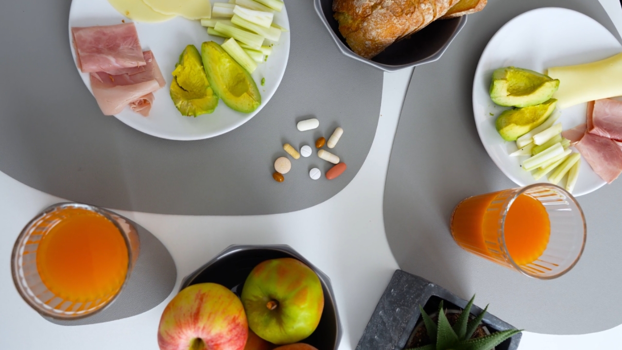 Doručak sa avokadom, voćem i sokom od pomorandže, uz nekoliko vitaminskih suplemenata na stolu.